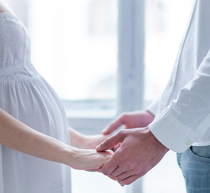 Married couple expecting a baby, holding hands in anticipation of the future